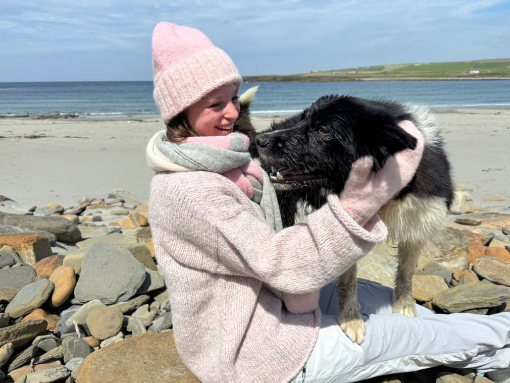 Model in alpacakledij op het strand met hond op schoot